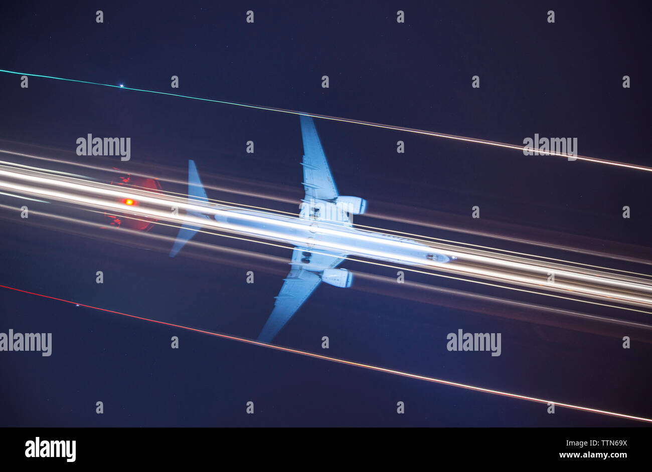 Low angle view of mât de signal contre light trails et avion dans le ciel de nuit Banque D'Images