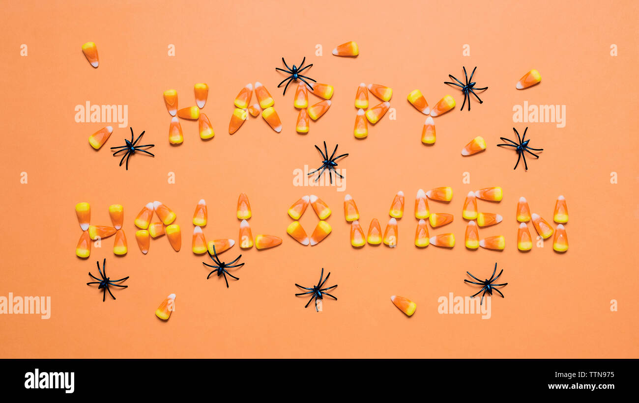 Vue de dessus de candy corns disposés comme Happy Halloween araignées artificielles au milieu de texte sur fond orange Banque D'Images