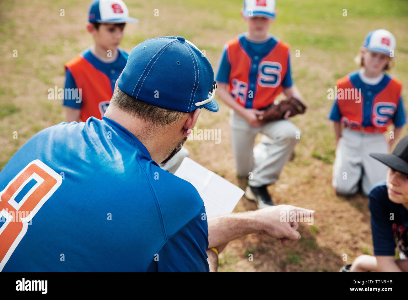 Vue arrière du coach pointant tout en discutant avec l'équipe de baseball sur terrain Banque D'Images