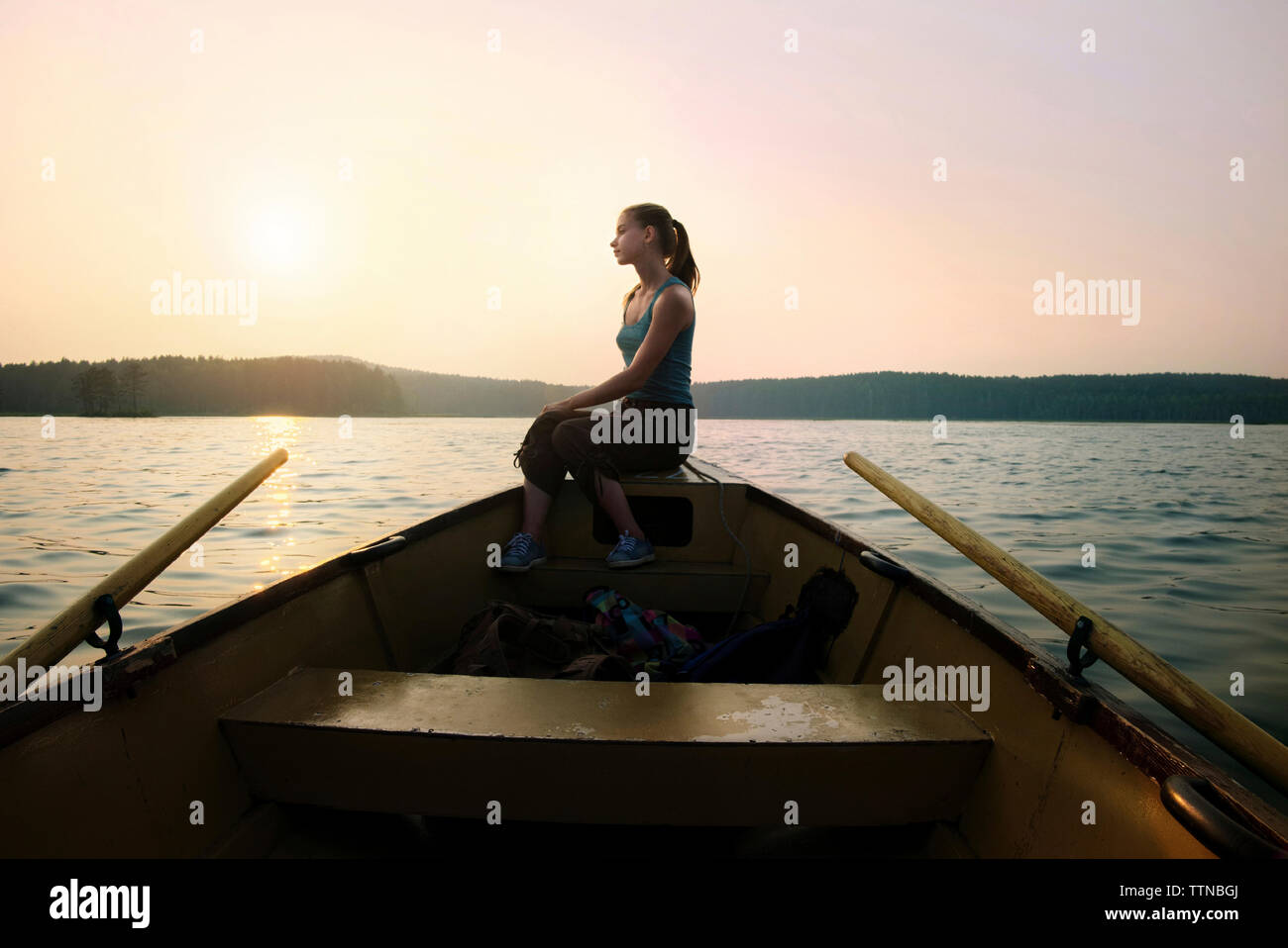 Une femme assise sur la proue du navire à canoe contre ciel clair pendant le crépuscule Banque D'Images