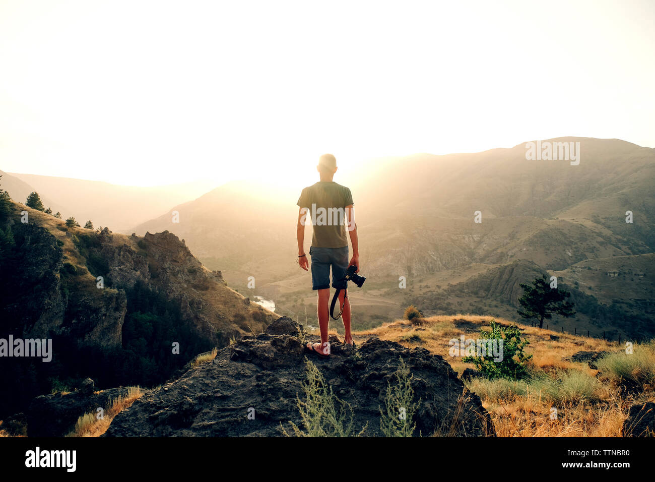 Vue arrière de l'appareil photo avec l'homme à la montagne en en étant debout sur rock against clear sky pendant le coucher du soleil Banque D'Images