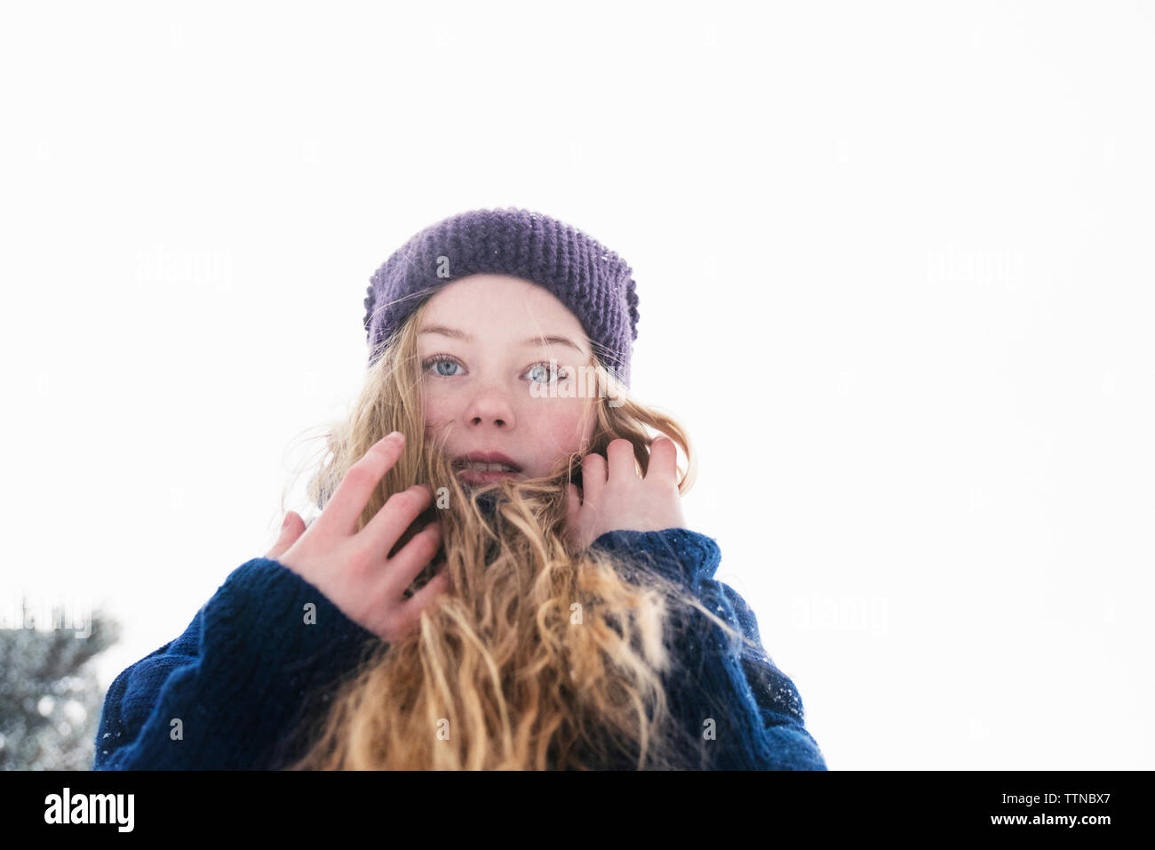 Low angle portrait de femme aux cheveux blonds debout contre un ciel clair au cours de l'hiver Banque D'Images