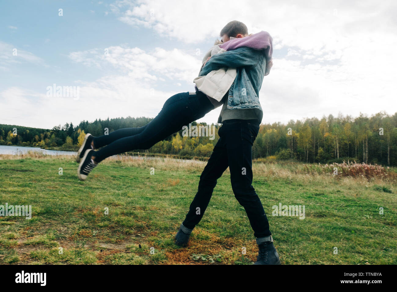 Low angle view of young couple embracing while standing on grassy field against cloudy sky in forest Banque D'Images