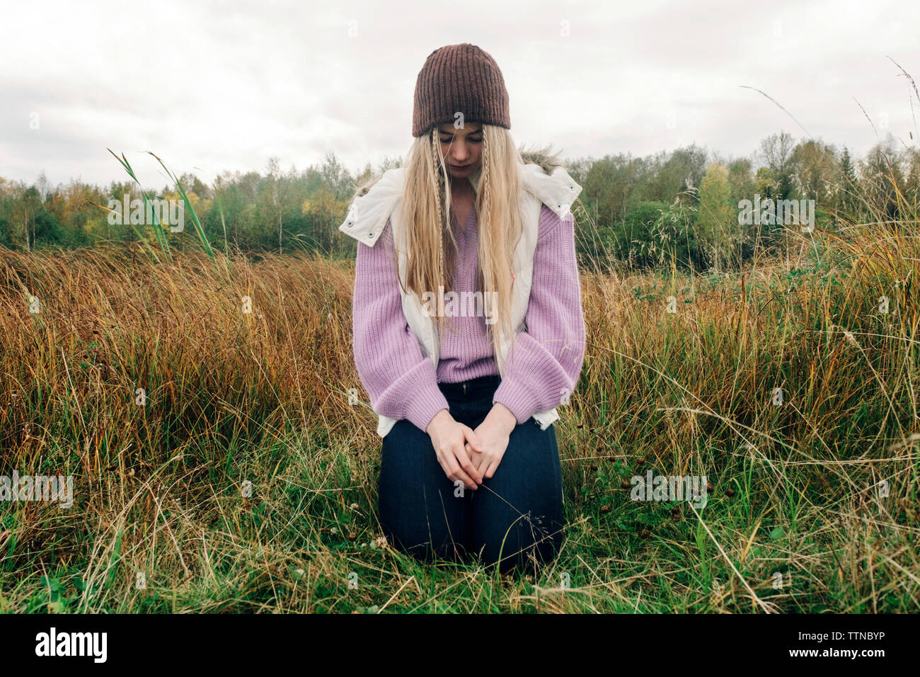 Femme aux cheveux blonds à genoux sur les champs contre ciel nuageux dans la forêt Banque D'Images