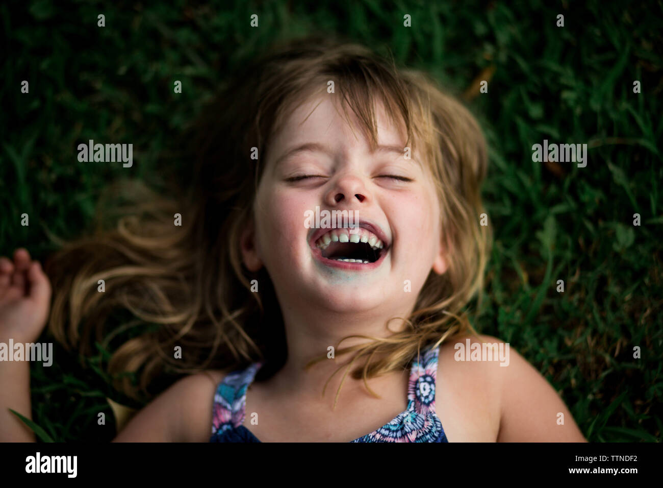 5 ans, fille, et rire avec les lèvres bleues de sucette, lying in grass Banque D'Images