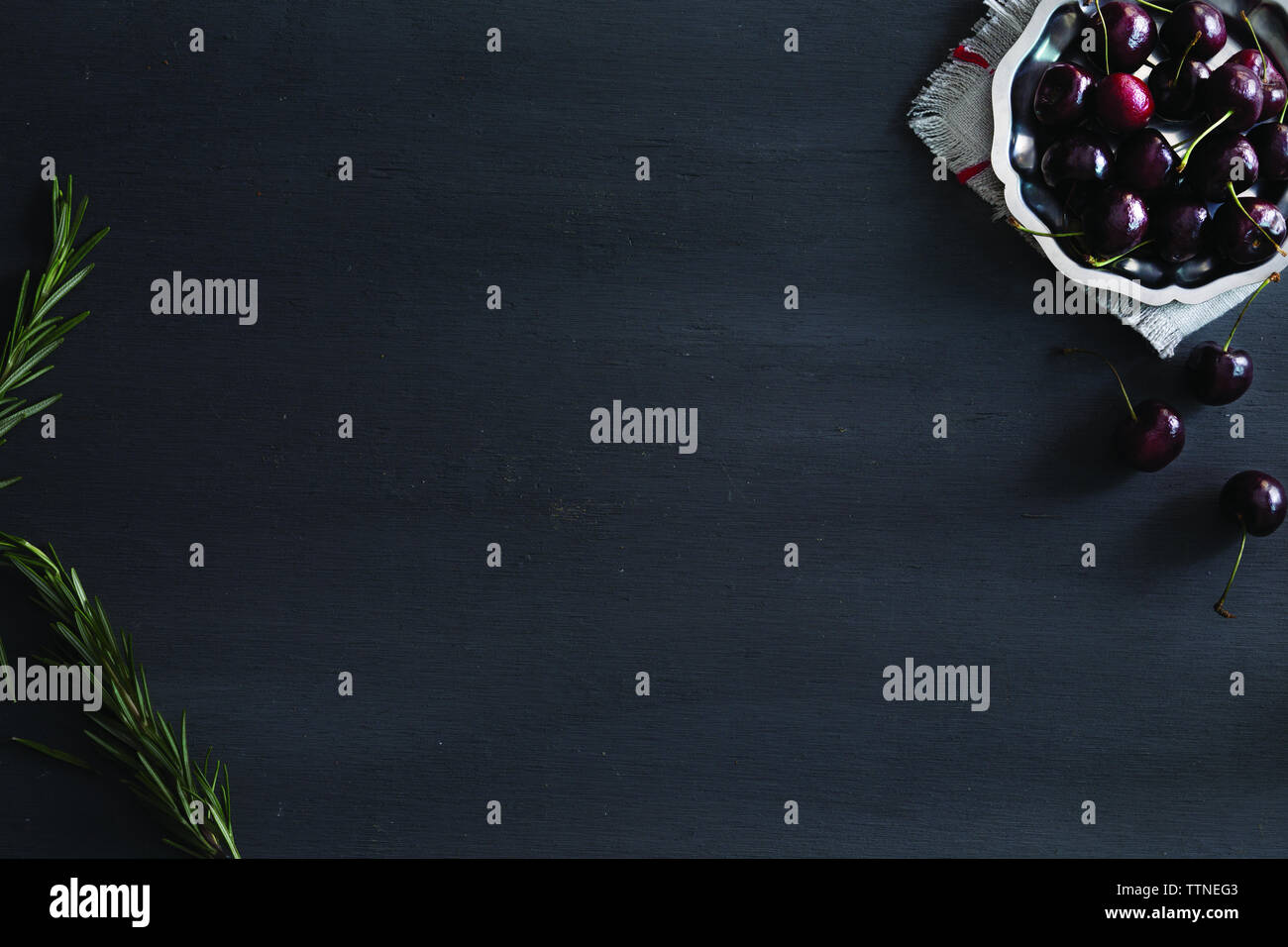 Vue en grand angle sur les cerises et le romarin sur une table noire Banque D'Images