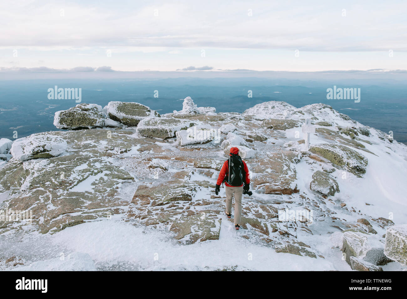 Vue arrière du backpacker avec caméra marche sur des roches couvertes de neige Banque D'Images