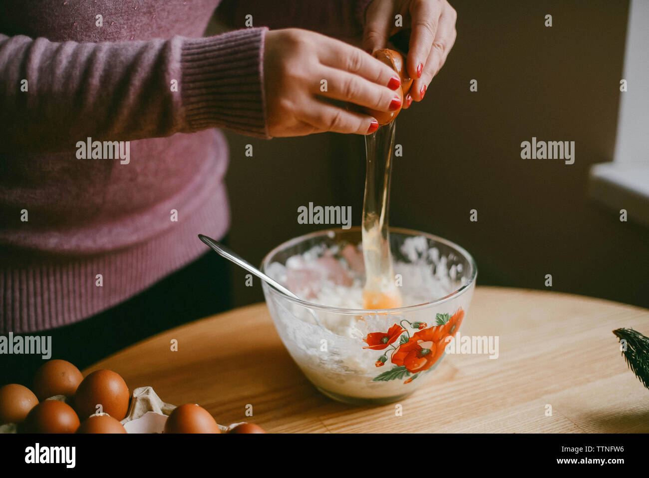 Midsection of woman breaking egg dans un bol sur la table en bois à la maison Banque D'Images
