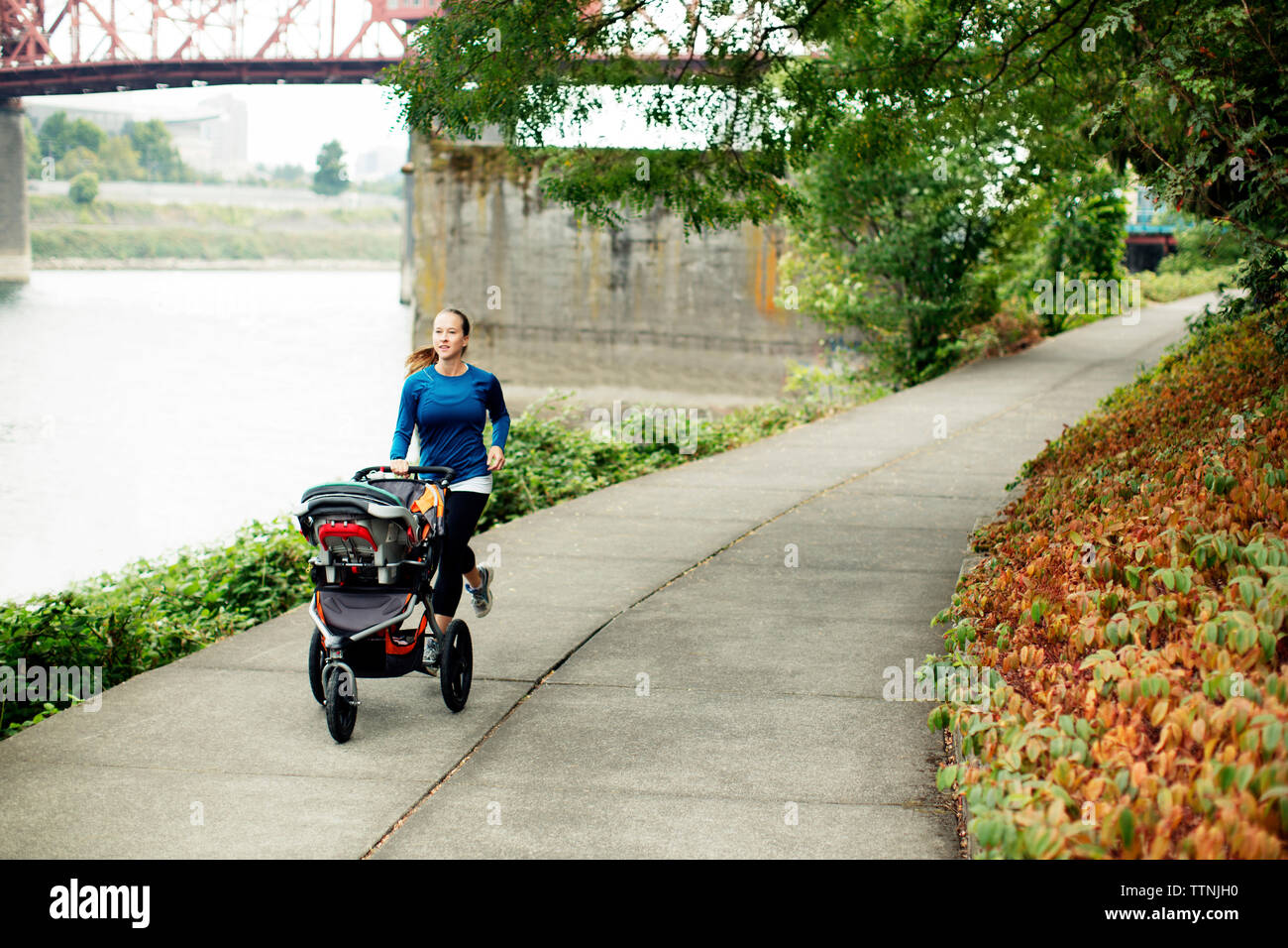 Jogging Femme avec poussette de bébé sur sentier par river Banque D'Images