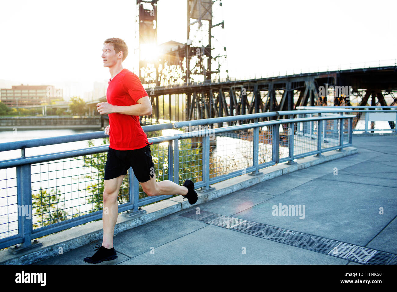 Vue latérale du man jogging on bridge contre ciel clair Banque D'Images
