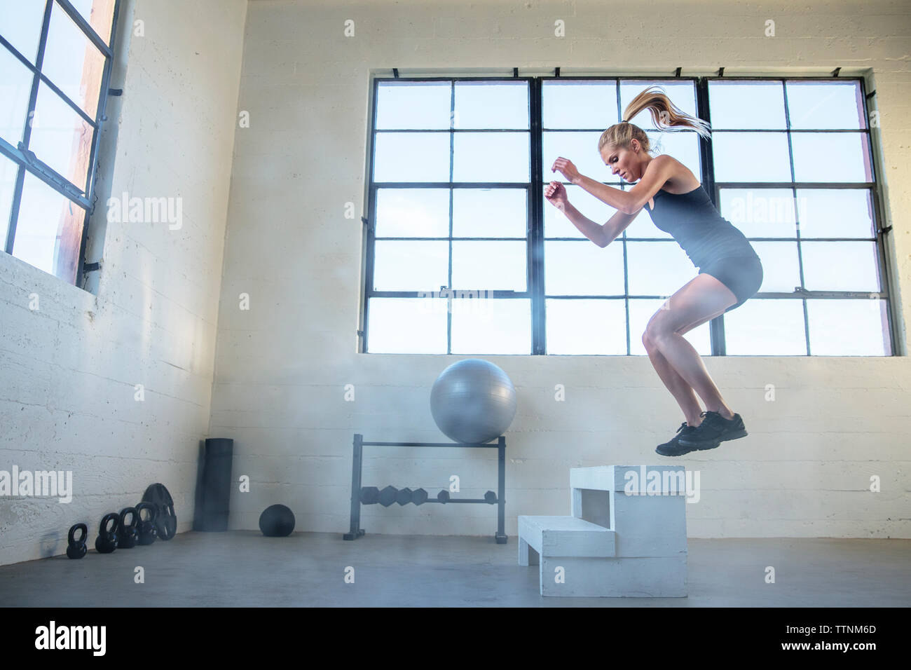 Toute la longueur du saut à l'athlète sur l'assise en bois dans une salle de sport Banque D'Images