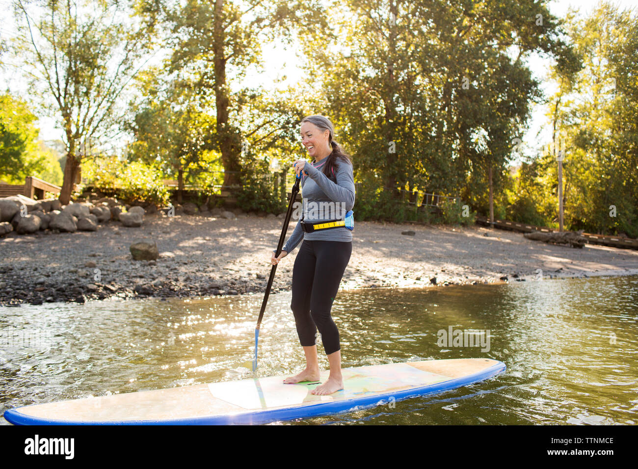 Toute la longueur de smiling woman paddleboarding sur river Banque D'Images