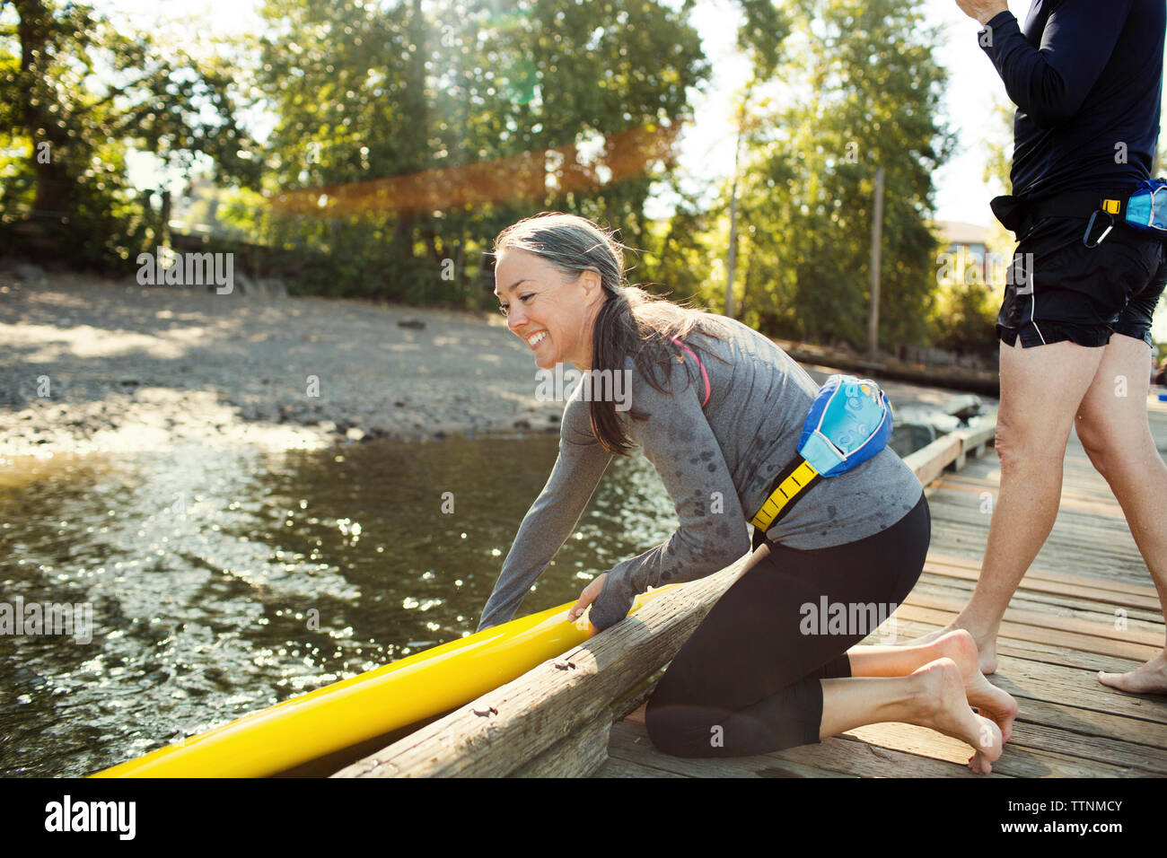 Femme plaçant paddleboard sur la rivière tandis que l'homme debout à côté du quai Banque D'Images