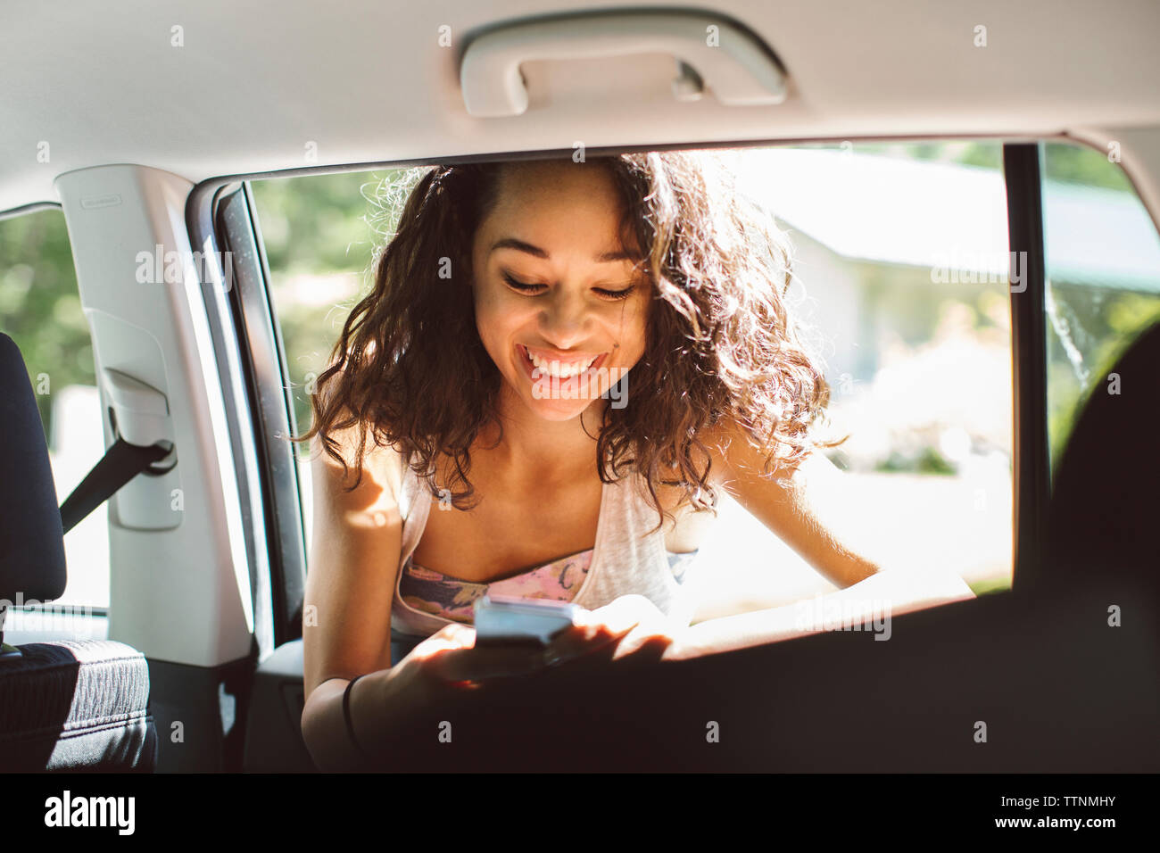 Smiling woman using mobile phone while leaning on car window Banque D'Images