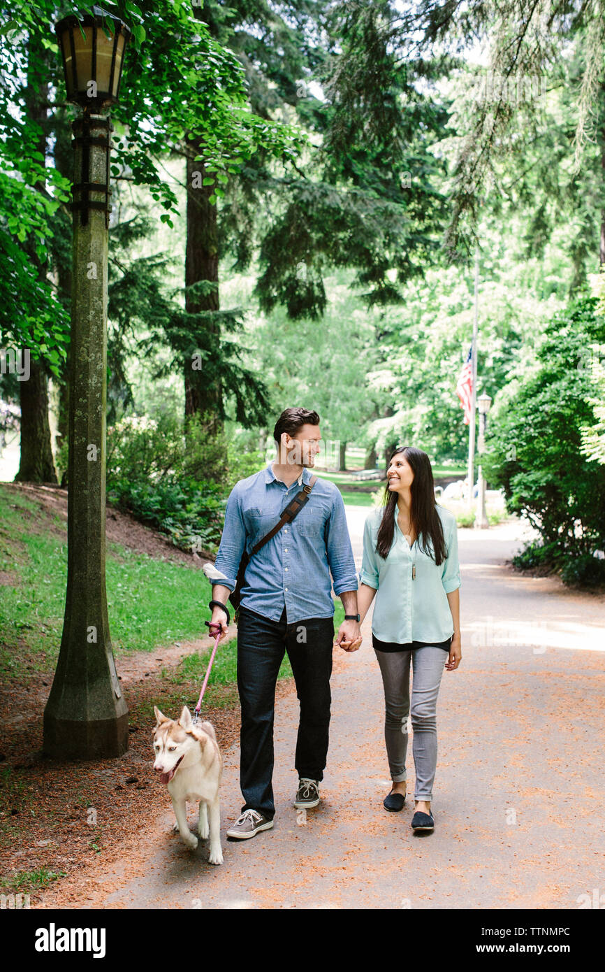 Heureux couple holding hands and walking sur sentier avec chien à park Banque D'Images