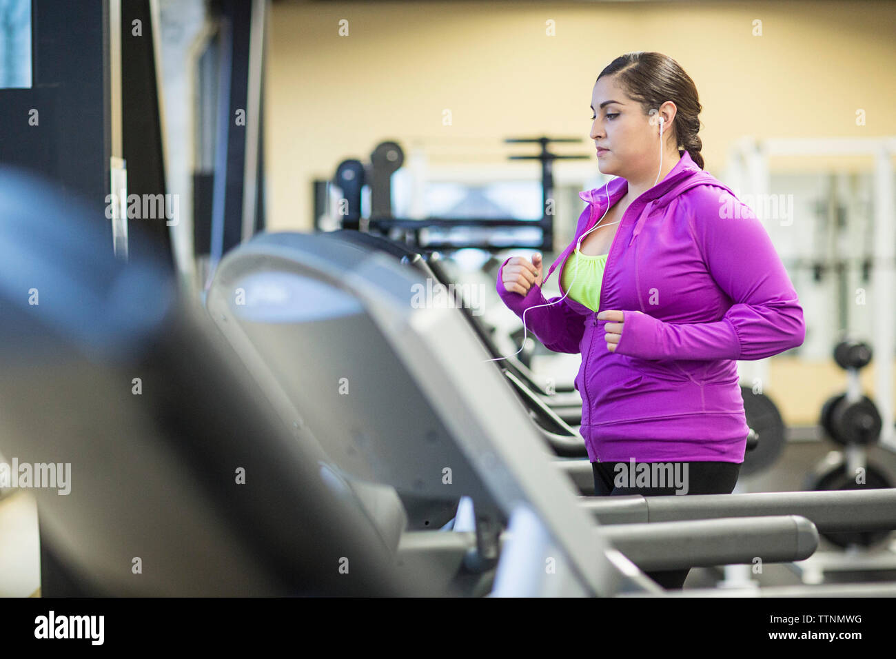 Woman listening music tout en exerçant le jogging sur tapis roulant dans une salle de sport Banque D'Images