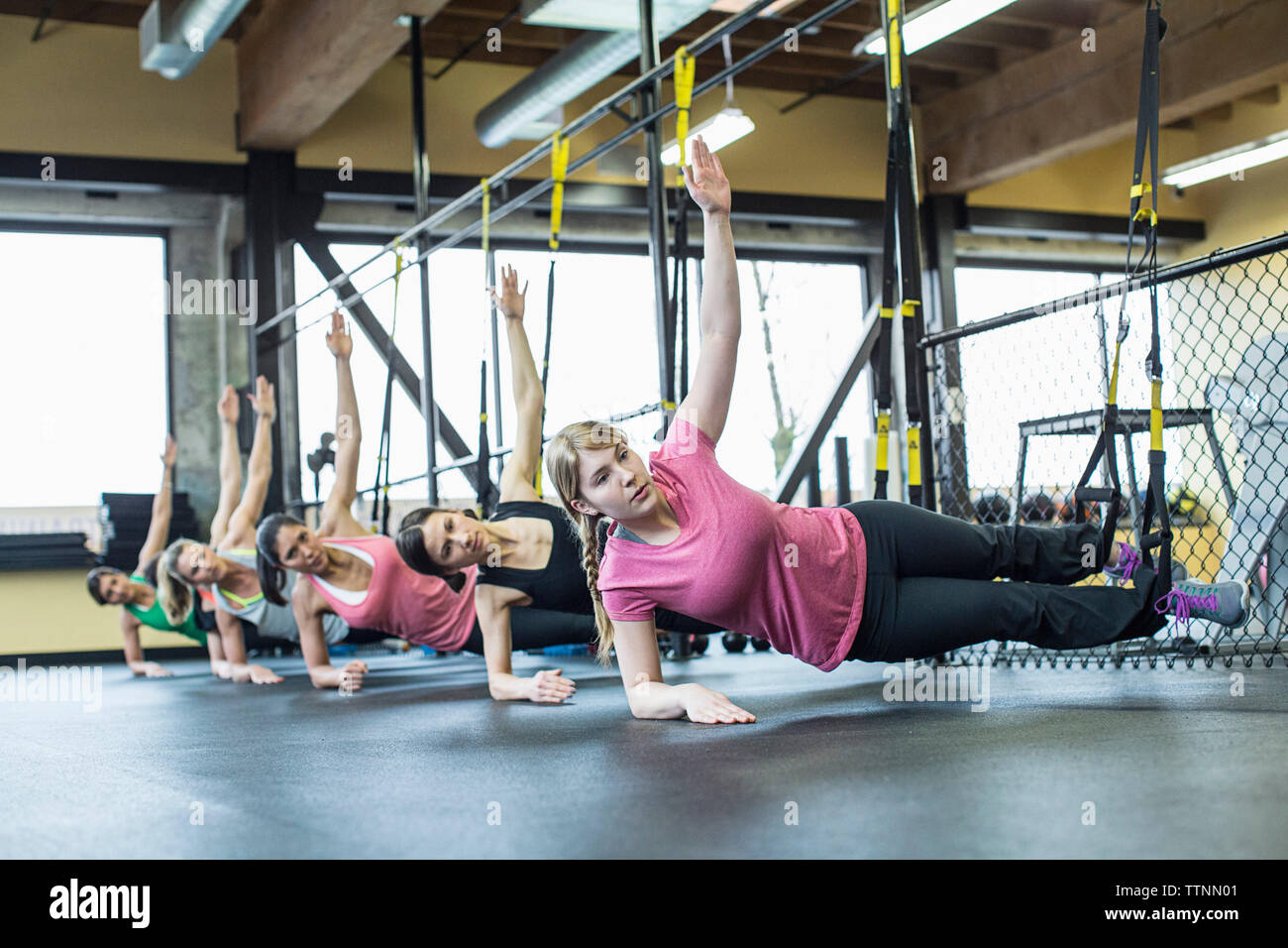 Du côté des femmes pratiquant planche tout en équilibrant sur bandes de résistance in gym Banque D'Images