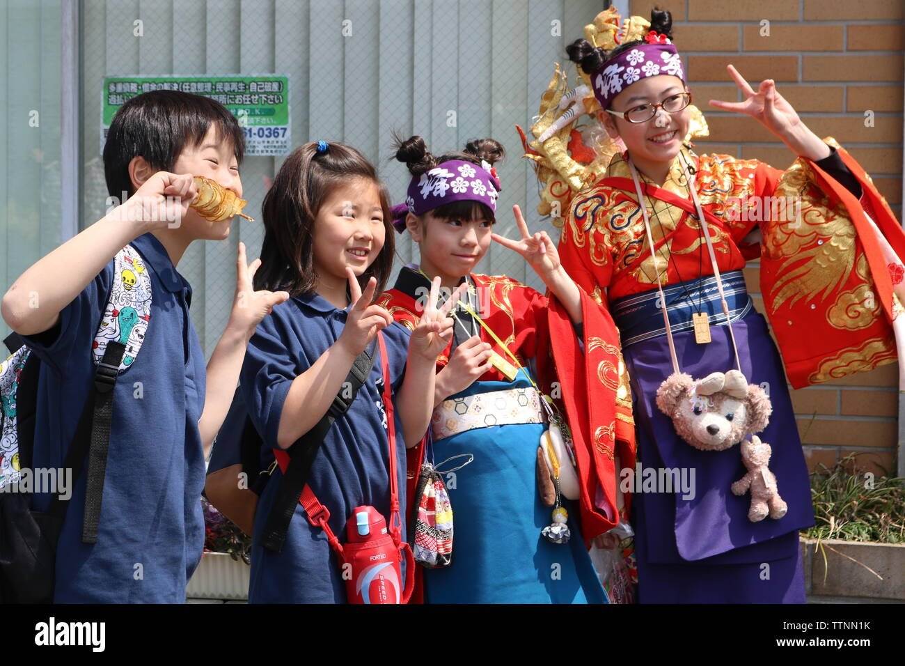 Quatre enfants japonais deux en robe moderne et deux kimonos en posant avec le geste de paix pīsu sain ou de deux doigts Banque D'Images