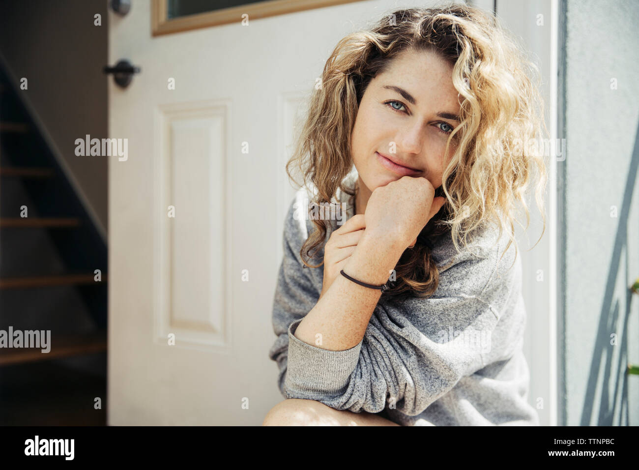 Portrait of smiling woman with hand on chin assis à la porte Banque D'Images