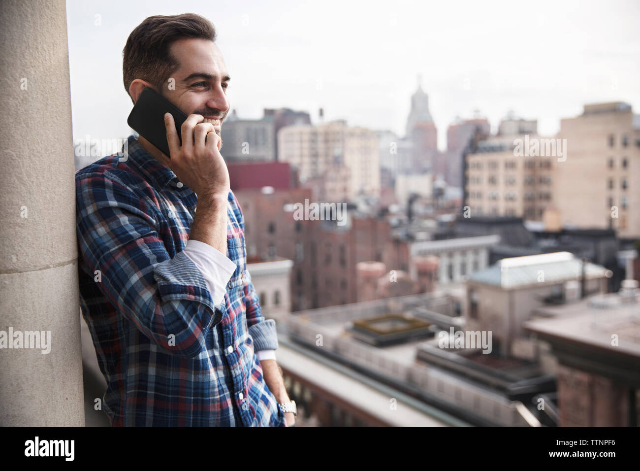 Smiling man talking on mobile phone while standing contre ville Banque D'Images