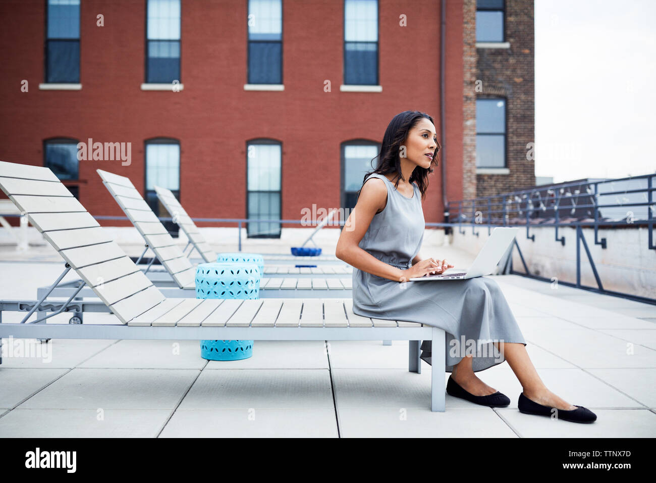 Thoughtful businesswoman with laptop computer assis sur chaise de salon en terrasse de l'immeuble Banque D'Images