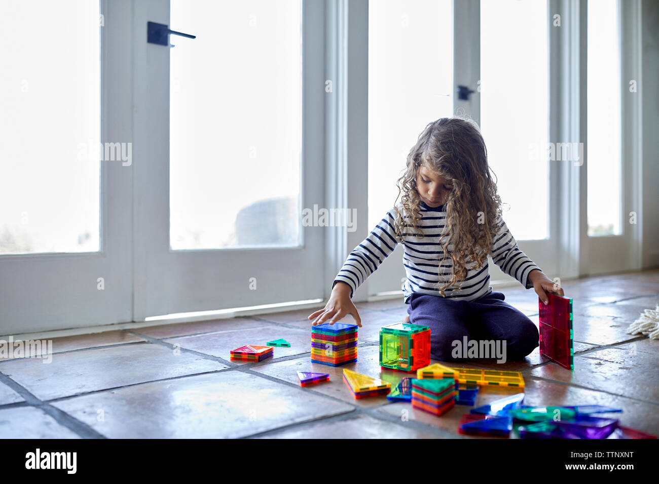 Cute girl Playing with toy blocks colorés tout en s'agenouillant sur le plancher à la maison Banque D'Images