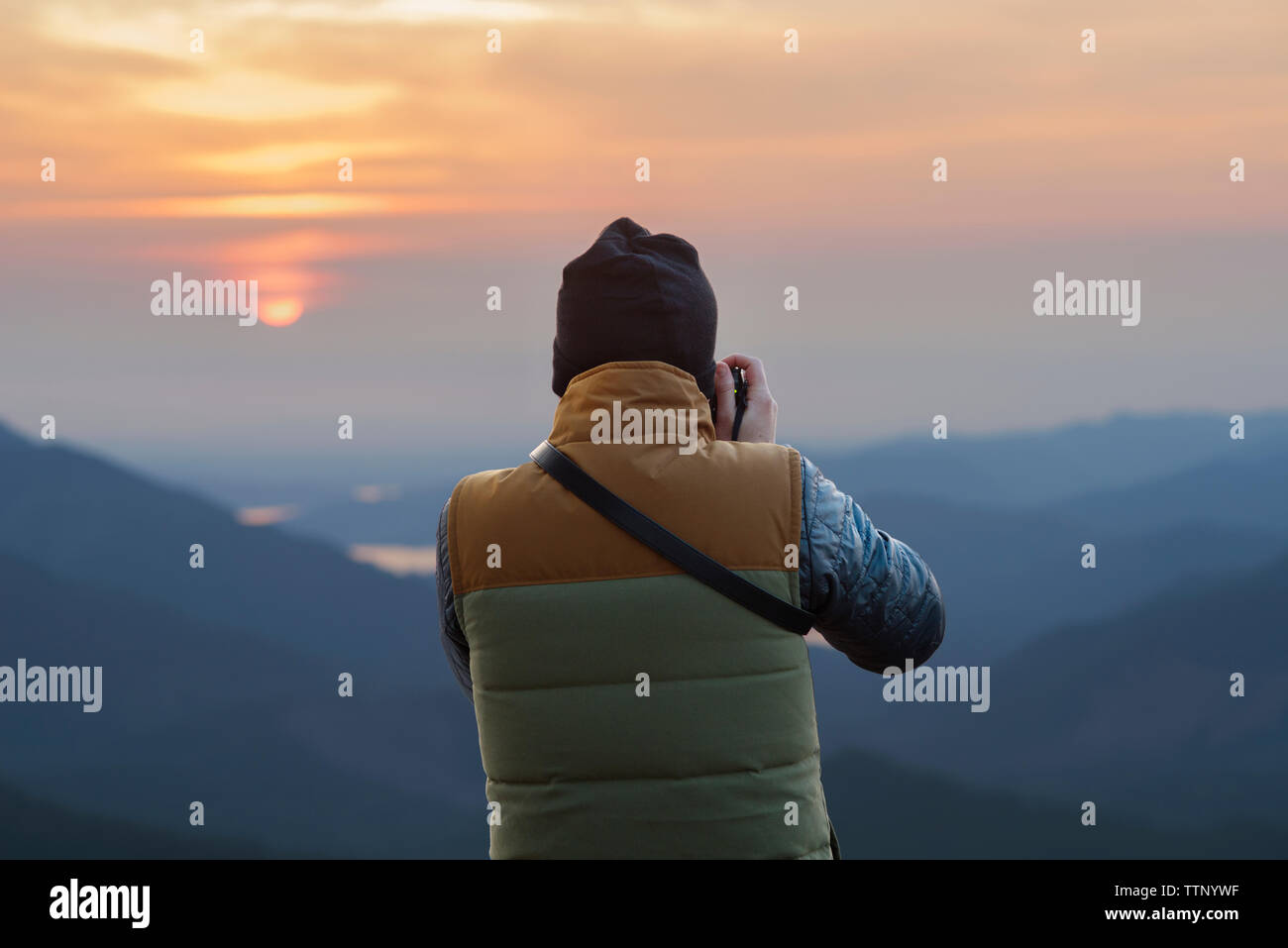 Vue arrière du male hiker photographing montagnes pendant le coucher du soleil Banque D'Images