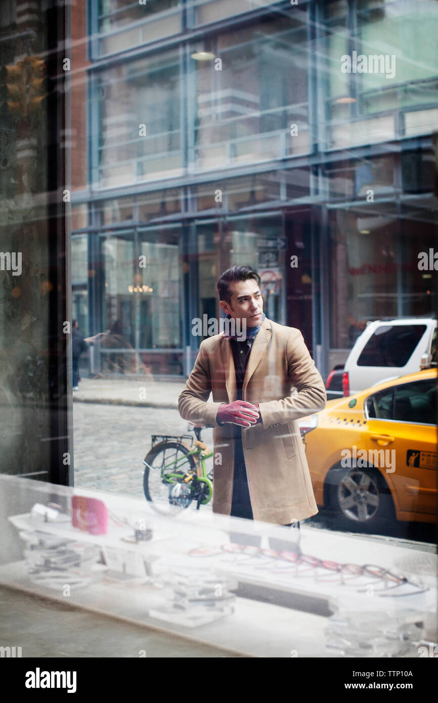 Homme debout sur le trottoir vu par fenêtre dans store Banque D'Images