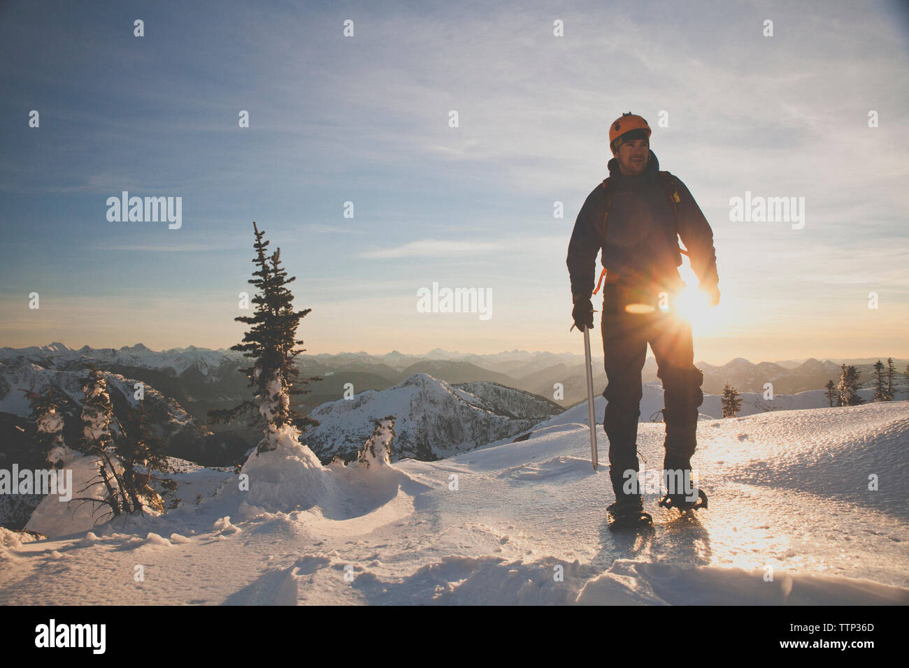 Toute la longueur du randonneur avec piolet alpinisme sur les montagnes couronnées de neige contre le ciel au coucher du soleil Banque D'Images