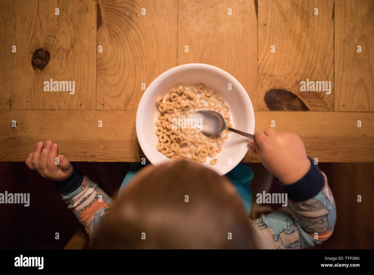 Vue de dessus de baby boy holding spoon en bol de petit-déjeuner sur la table en bois à la maison Banque D'Images