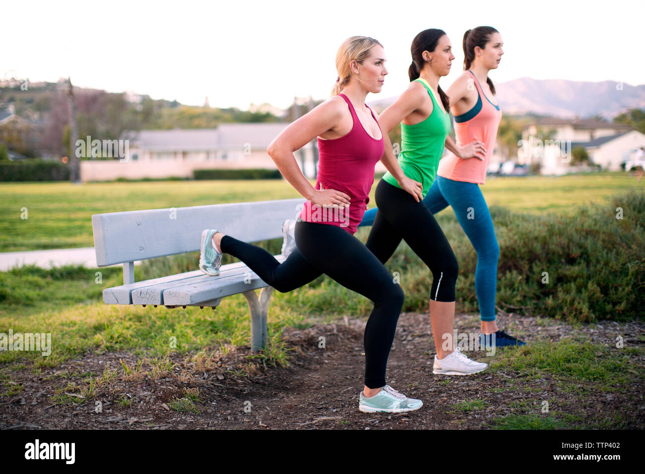 Les femmes exerçant sur banc de parc sur terrain Banque D'Images