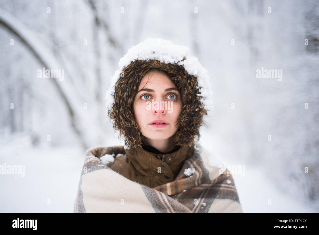 Jeune fille enveloppée dans une couverture dans la forêt enneigée regarde au loin dans la distance Banque D'Images