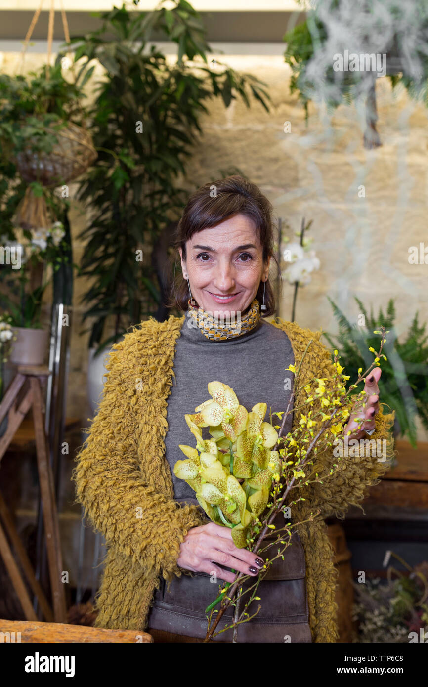 Portrait of smiling senior woman holding fleurs jaunes à flowershop Banque D'Images