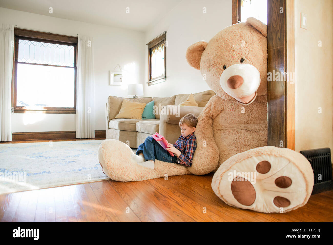 Vue latérale du jeu garçon assis sur Grand ours en peluche à la maison Banque D'Images