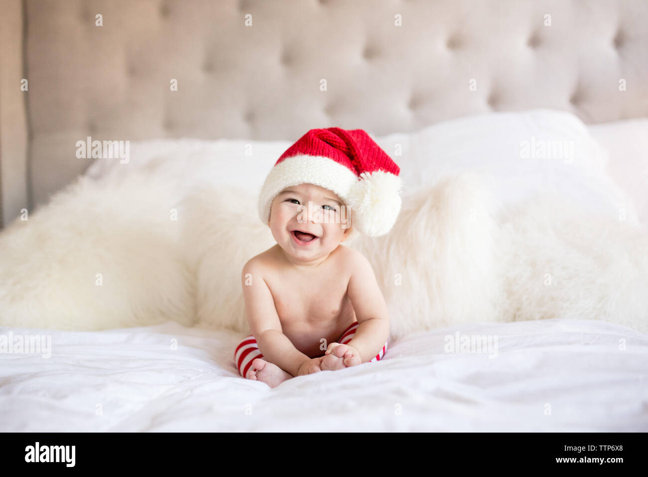 Happy smiling cute baby boy wearing Santa hat sur le lit à l'intérieur Banque D'Images