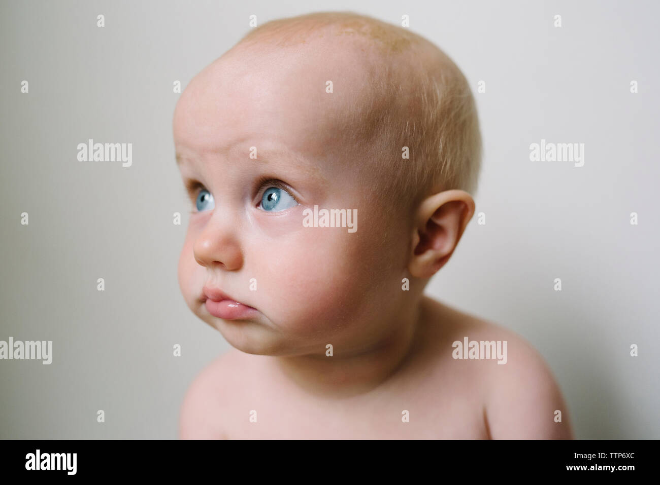 Cute baby girl looking away against wall Banque D'Images