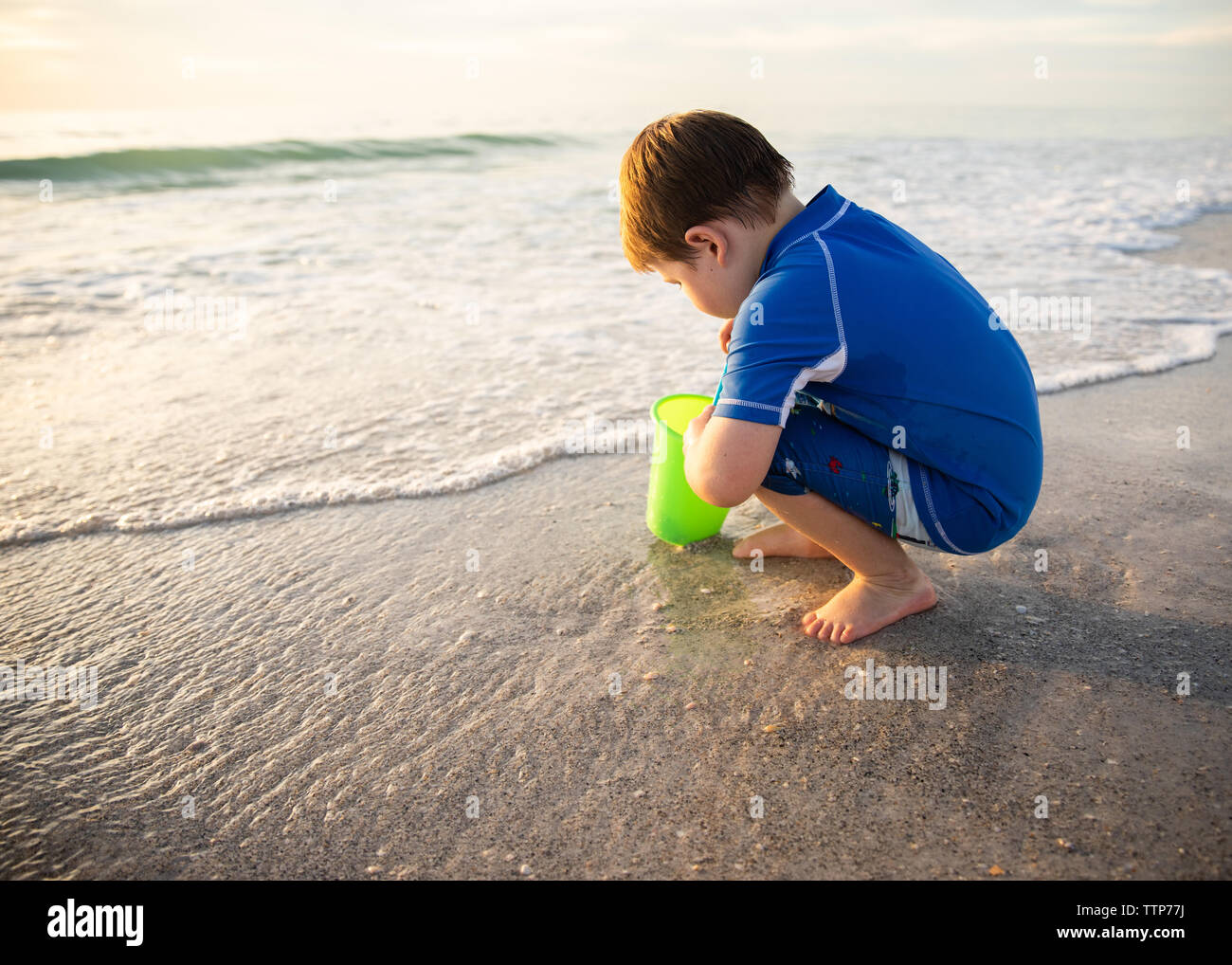 Enfant à genoux avec godet à la recherche de coquillages sur la rive Banque D'Images
