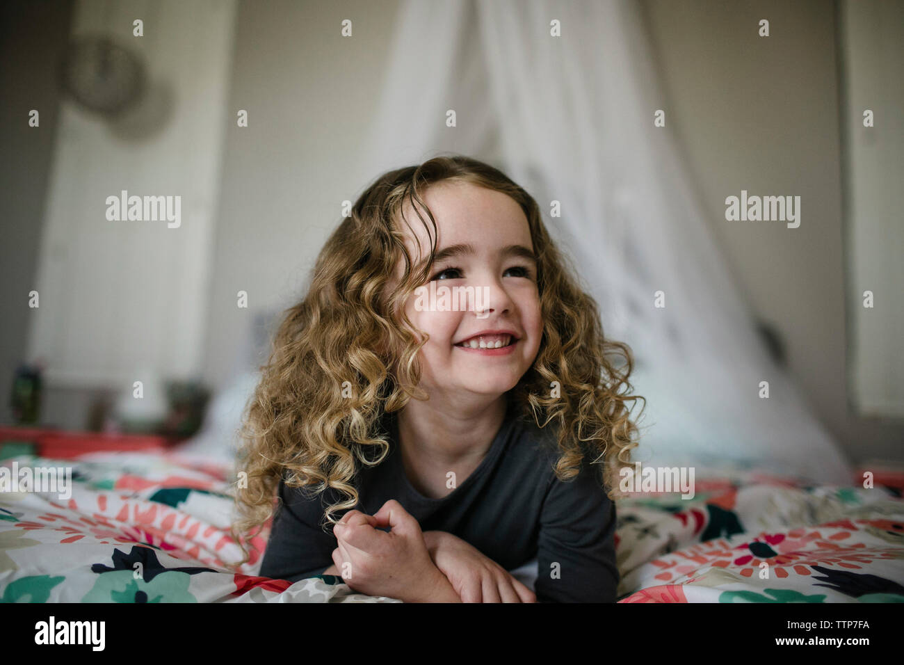 Cute cheerful girl looking away while lying on bed at home Banque D'Images