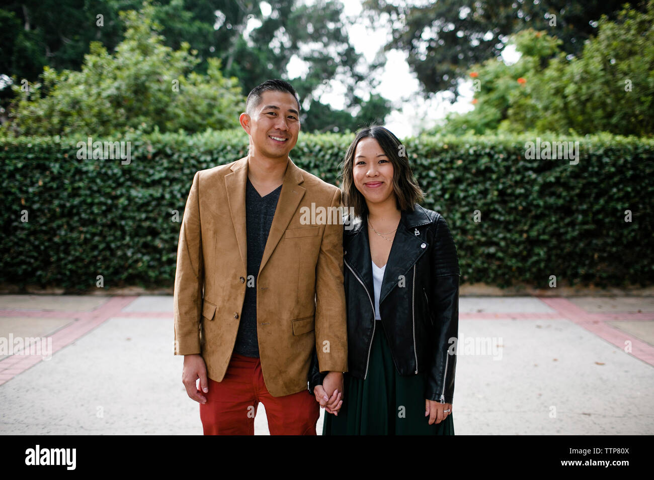 Portrait of happy couple holding hands en se tenant sur le trottoir contre des plantes à Balboa Park Banque D'Images