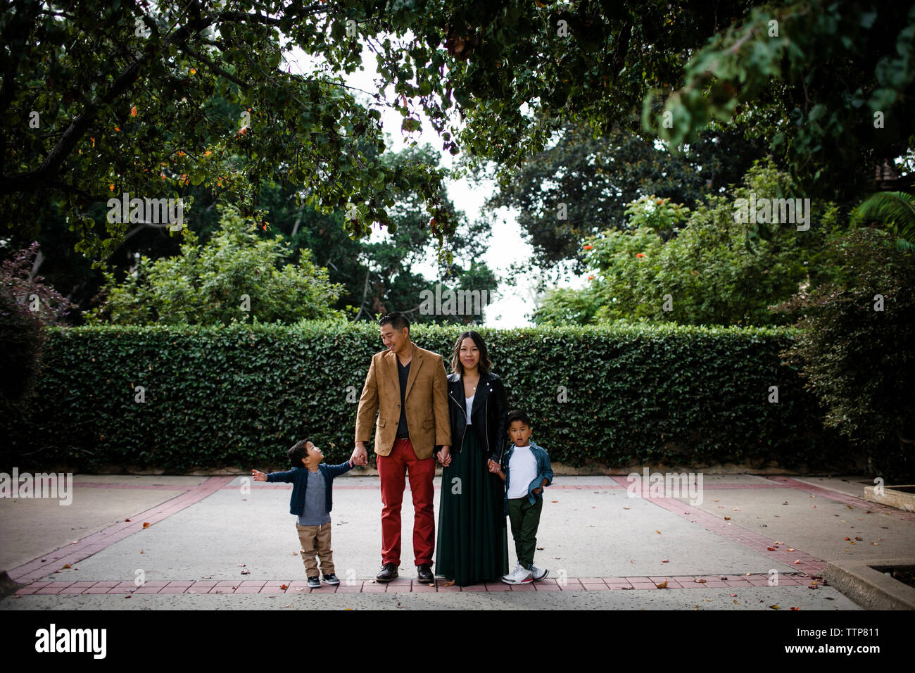 Smiling parents tenant la main d'adorables fils en se tenant sur le trottoir contre des plantes à Balboa Park Banque D'Images