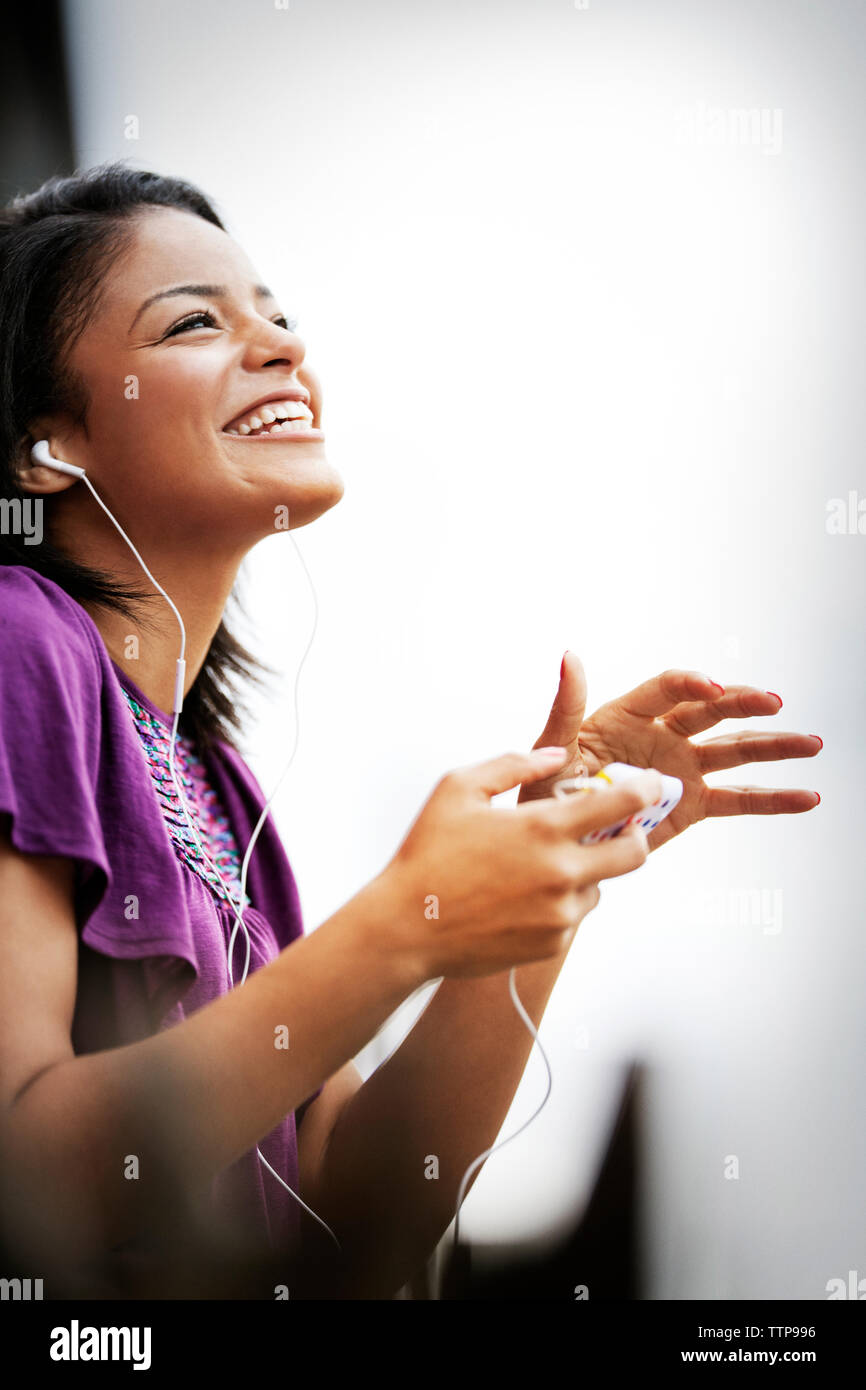 Femme souriante avec des écouteurs et smart phone against sky Banque D'Images