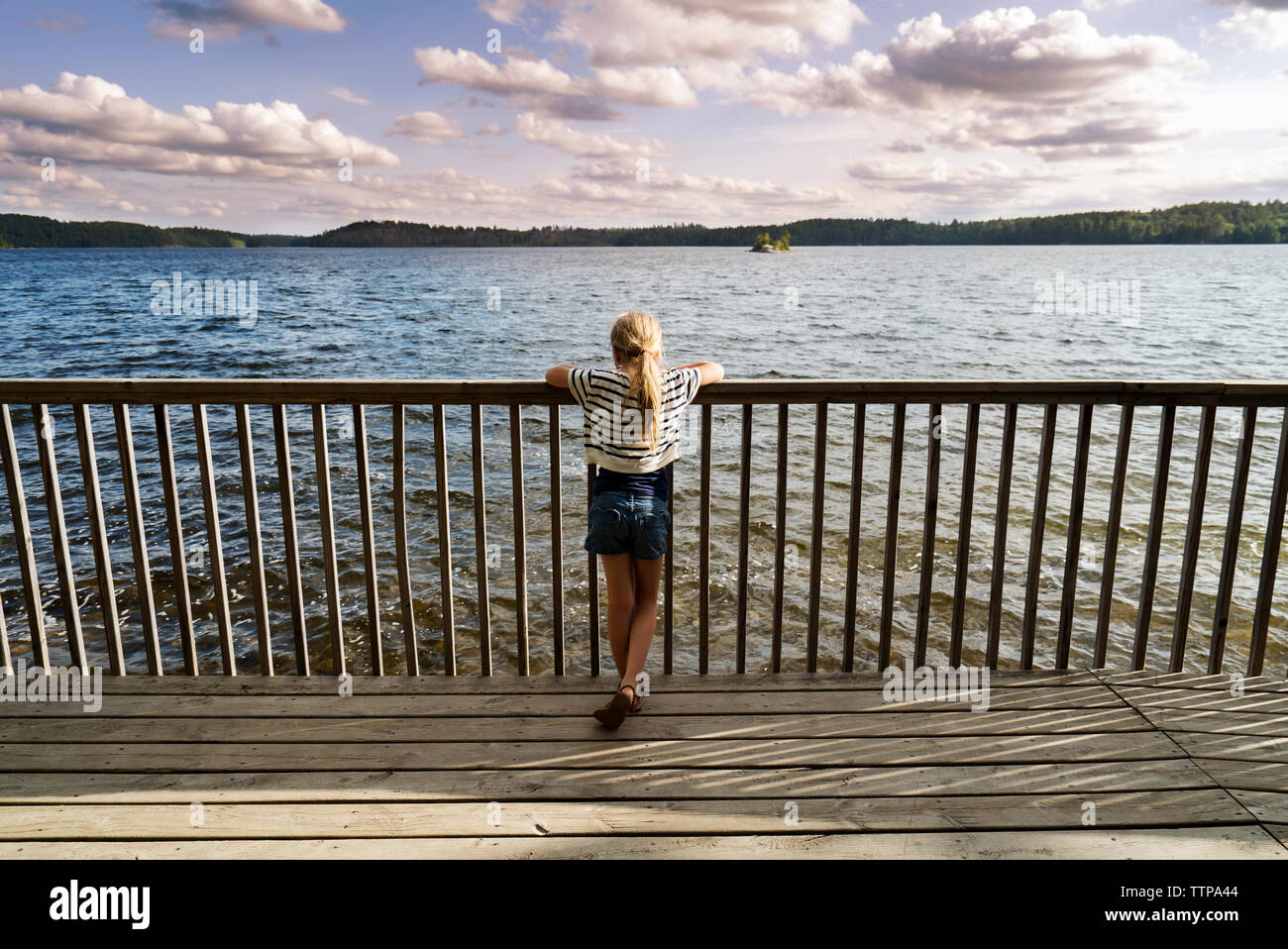 Vue arrière du Girl standing on jetty by railing sur le lac et à la vue de Banque D'Images