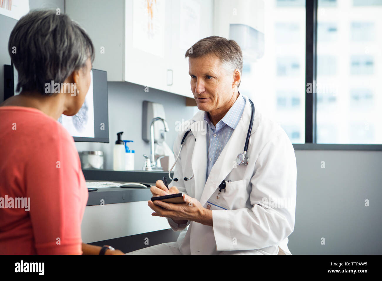 Médecin homme écrit dans notes tout en discutant avec female patient in clinic Banque D'Images