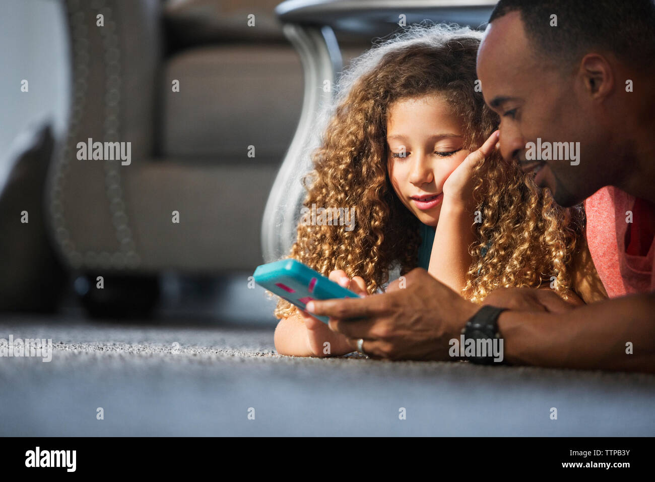 Père et fille jouer jeu de poche en position couchée sur un tapis à la maison Banque D'Images