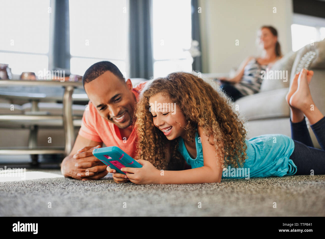 Heureux père et fille jouer jeu de poche en position couchée sur le plancher à la maison Banque D'Images