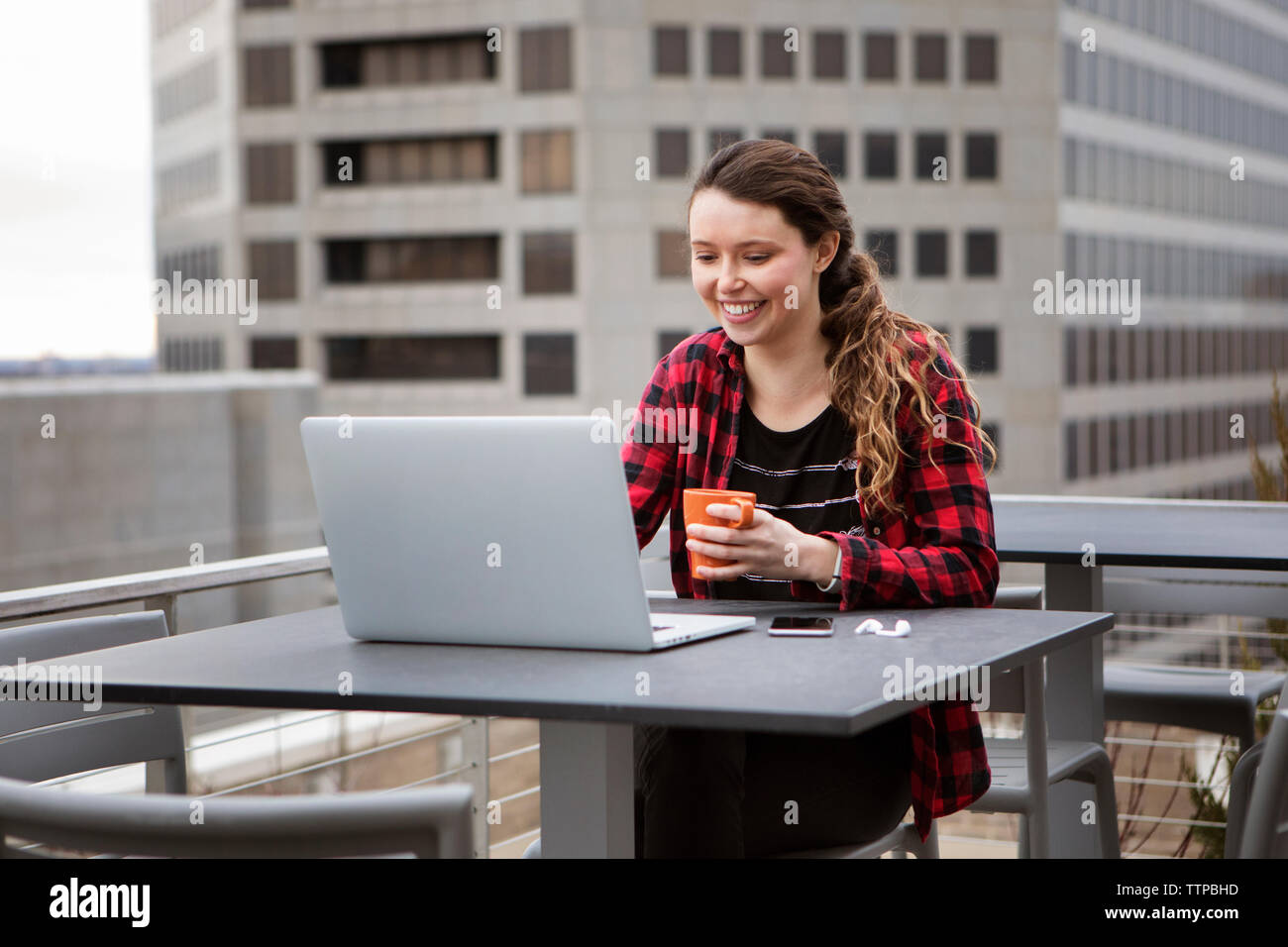 Smiling young woman using laptop computer assis à Terrace cafe Banque D'Images
