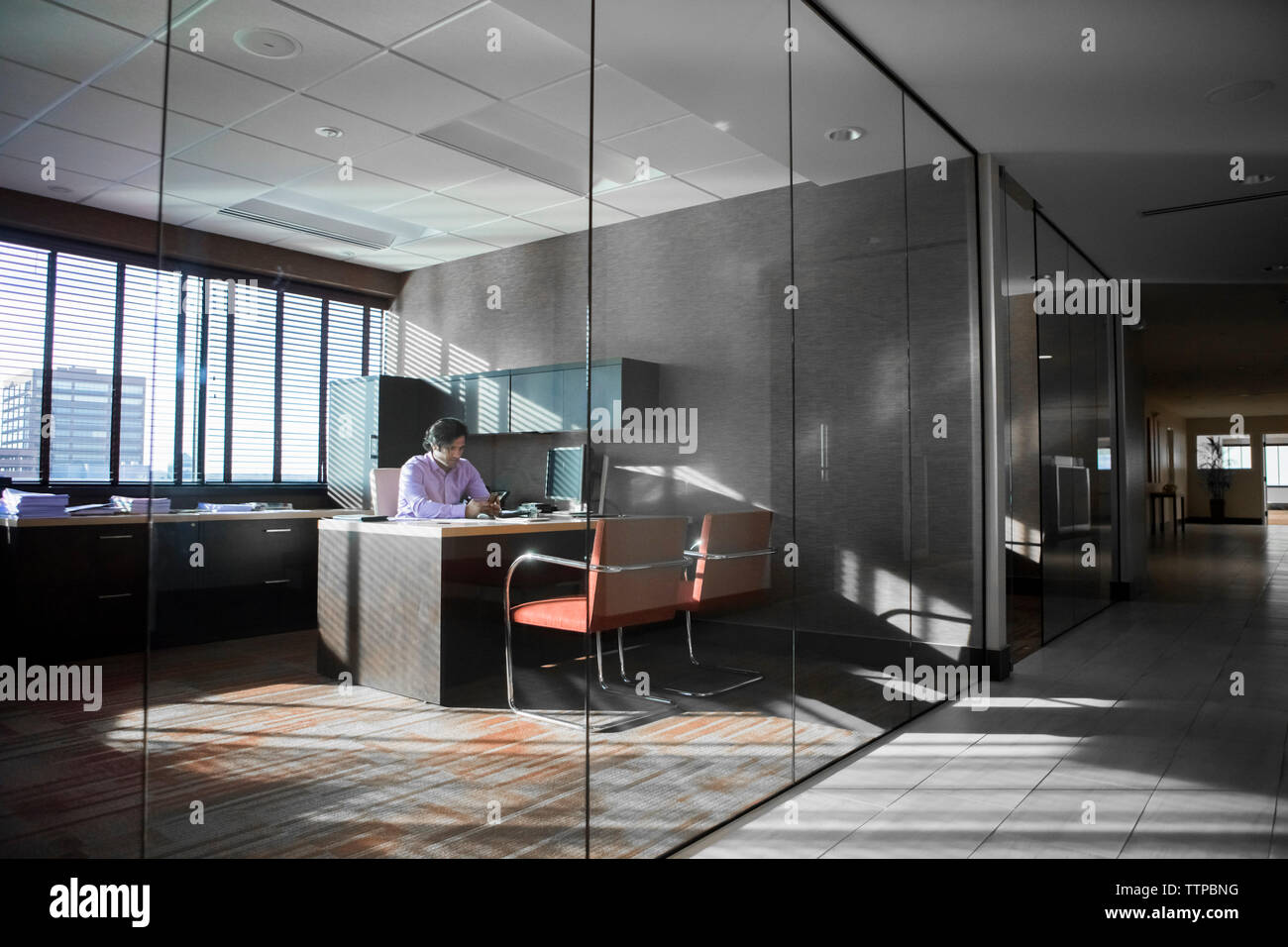 homme d'affaires utilisant le téléphone intelligent au bureau dans le bureau vu à travers le verre Banque D'Images