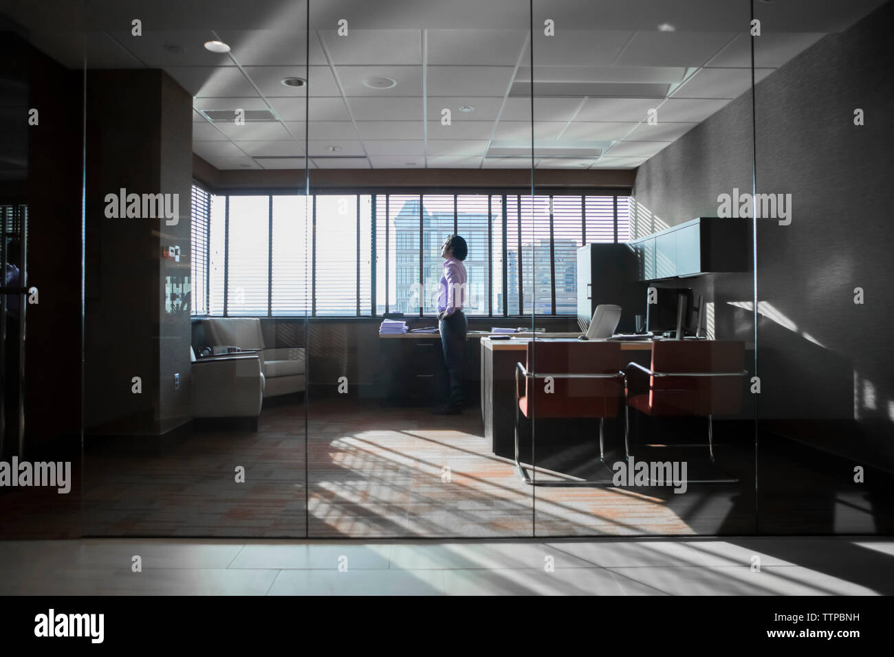 homme d'affaires parlant sur téléphone intelligent par fenêtre dans le bureau vu à travers le verre Banque D'Images