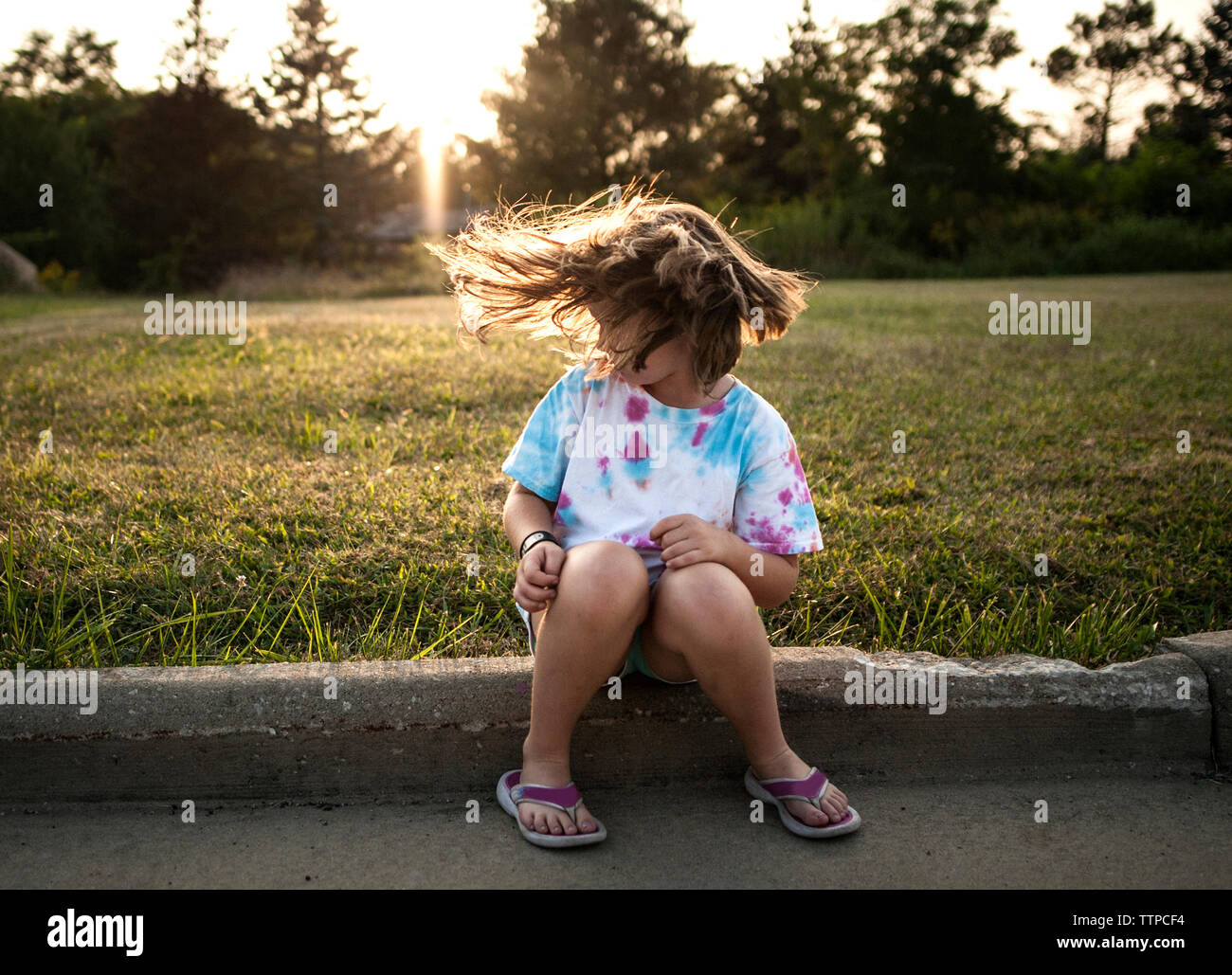 Playful girl tossing cheveux alors assis à park pendant le coucher du soleil Banque D'Images