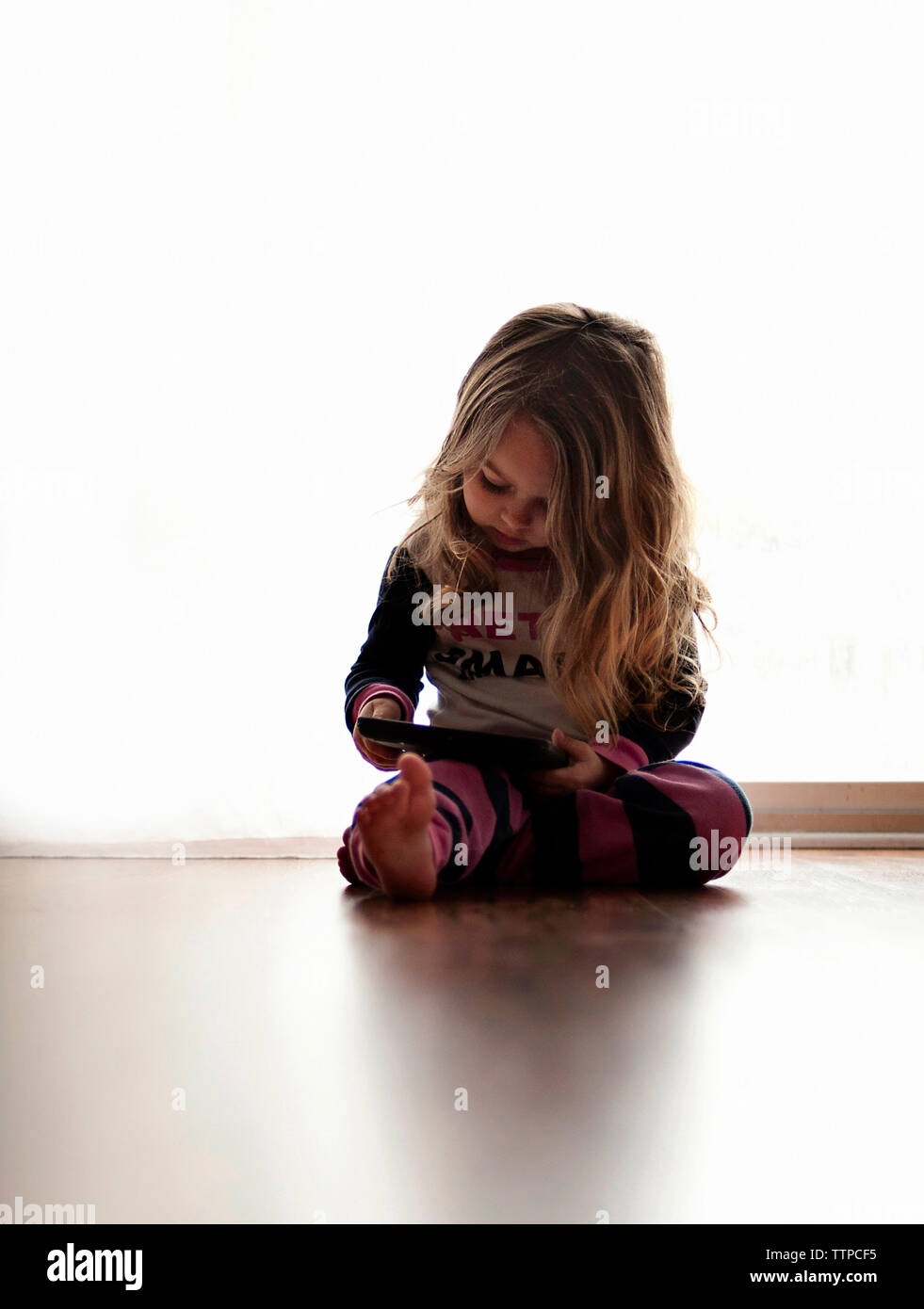 Girl using tablet computer, assis sur le plancher contre rideau à Accueil Banque D'Images